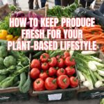 A close-up, vibrant photograph of a farmers market table piled high with colorful fresh produce, including leeks, tomatoes, orange carrots, green broccoli, and red bell peppers, illustrating how to keep produce fresh for a plant-based diet.