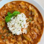 Close-up of a bowl of Vegan Cabbage Soup with tender cabbage ribbons, vegan ground beef, and a scoop of white rice in a rich tomato broth.