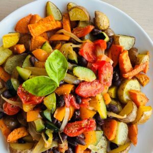A plate filled with vegan sweet potato hash, featuring roasted potatoes, black beans, bell peppers, and fresh basil garnish.
